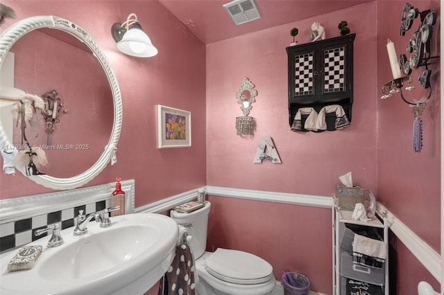 half bathroom with a sink, toilet, and visible vents