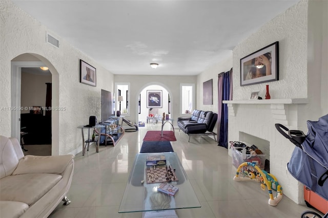living room with arched walkways, a textured wall, tile patterned flooring, and visible vents