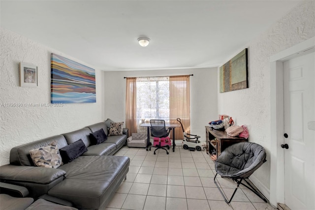 living area with baseboards, a textured wall, and light tile patterned flooring