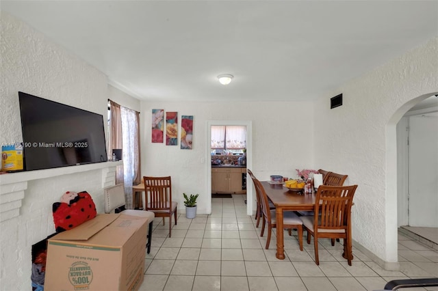 dining area with light tile patterned floors, arched walkways, a textured wall, and visible vents