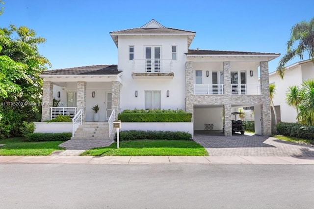 view of front of house featuring a balcony, stone siding, decorative driveway, stucco siding, and a porch