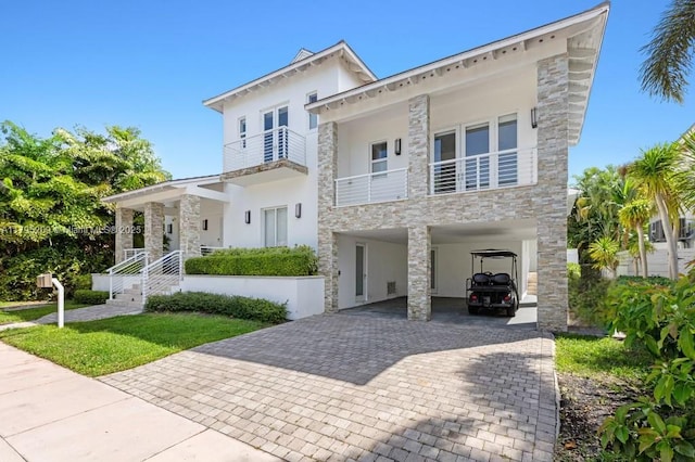 italianate home featuring stone siding, stucco siding, decorative driveway, a balcony, and a carport