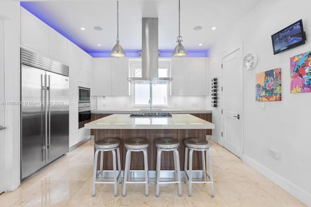 kitchen featuring a kitchen breakfast bar, island exhaust hood, a center island, built in appliances, and white cabinetry