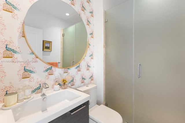 bathroom with toilet, wallpapered walls, a shower stall, and vanity