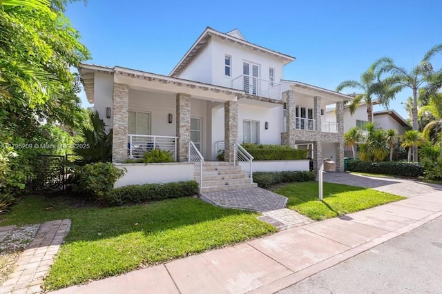 mediterranean / spanish home featuring a front lawn, stone siding, stucco siding, a balcony, and covered porch
