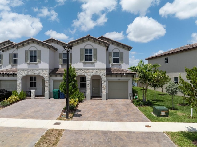 view of front facade with decorative driveway, a garage, a tile roof, and stucco siding