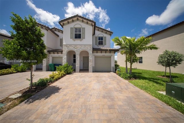 mediterranean / spanish house featuring an attached garage, stone siding, stucco siding, decorative driveway, and a tiled roof