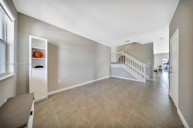 empty room with tile patterned flooring, baseboards, and stairway