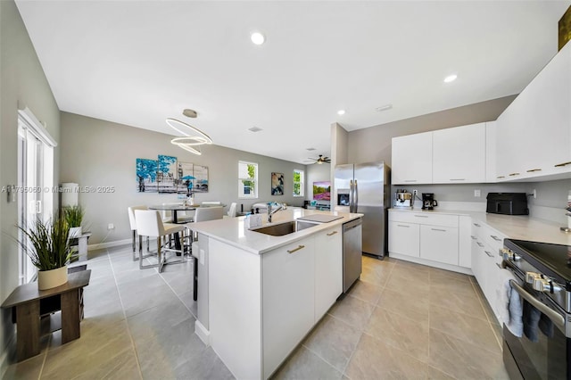 kitchen featuring white cabinets, appliances with stainless steel finishes, a sink, light countertops, and an island with sink