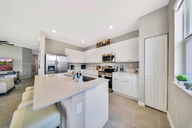 kitchen featuring a breakfast bar, white cabinetry, a sink, light tile patterned floors, and stainless steel appliances