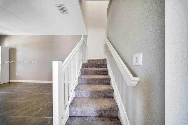 staircase with tile patterned flooring, a textured wall, and visible vents