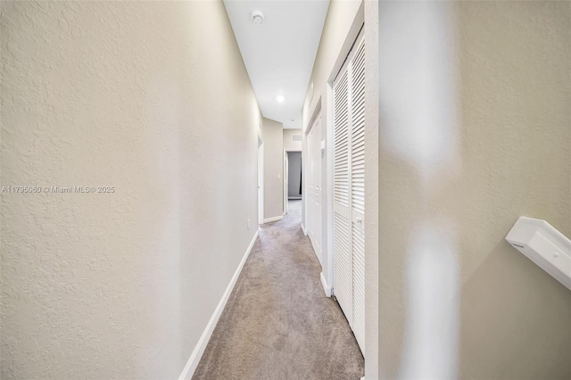 hall featuring baseboards, carpet flooring, and a textured wall