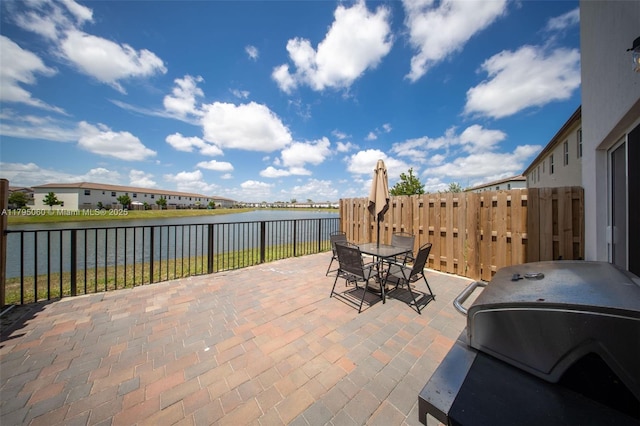 view of patio featuring outdoor dining area, a water view, fence, and grilling area