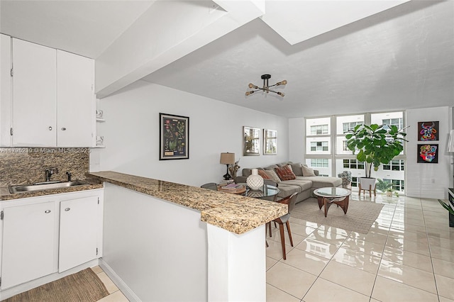 kitchen with a peninsula, light tile patterned flooring, white cabinetry, tasteful backsplash, and a sink