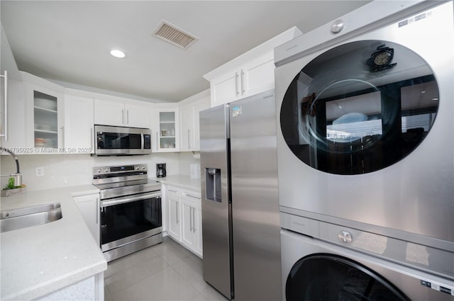 kitchen with visible vents, a sink, light countertops, stacked washer and clothes dryer, and stainless steel appliances