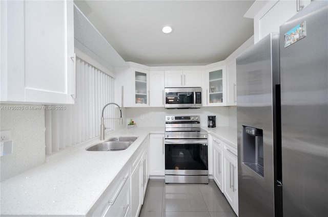 kitchen with glass insert cabinets, white cabinetry, tile patterned floors, a sink, and appliances with stainless steel finishes