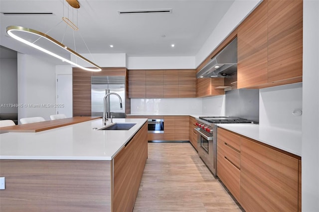 kitchen featuring high end appliances, modern cabinets, ventilation hood, brown cabinets, and a sink
