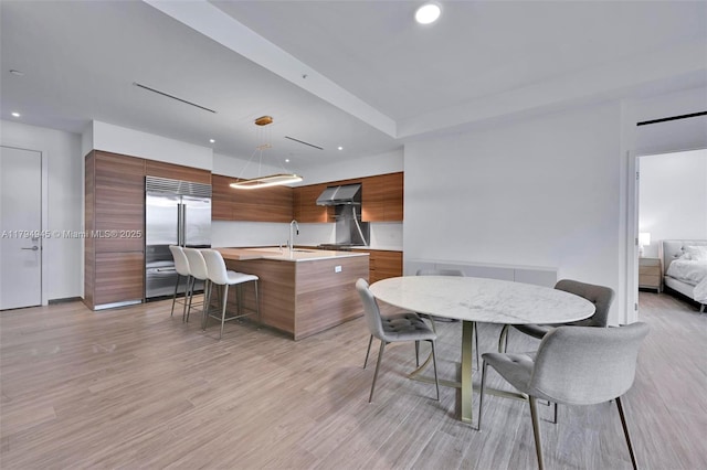 kitchen featuring wall chimney range hood, built in refrigerator, modern cabinets, and light countertops