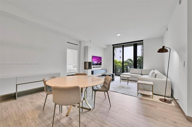 3581 E Glencoe St Unit 207, Miami, FL 33133 - dining space with baseboards, a wall of windows, and light wood finished floors