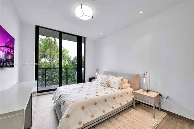 bedroom featuring a wall of windows, baseboards, multiple windows, and light wood-type flooring