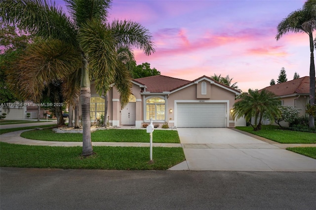 view of front of house with a lawn, driveway, a tiled roof, an attached garage, and stucco siding