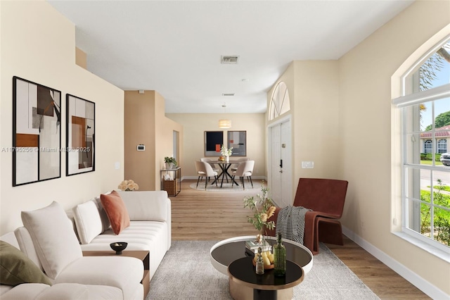 living area featuring a healthy amount of sunlight, baseboards, visible vents, and wood finished floors