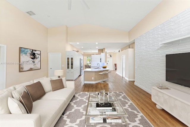 living room featuring light wood-style floors, visible vents, lofted ceiling, and ceiling fan