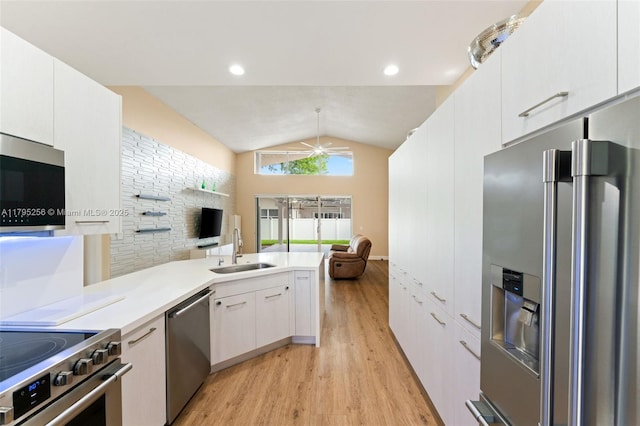 kitchen with a sink, vaulted ceiling, light wood finished floors, open floor plan, and appliances with stainless steel finishes