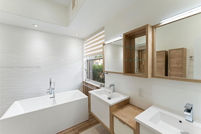 full bathroom featuring a sink, two vanities, tile walls, a freestanding tub, and recessed lighting