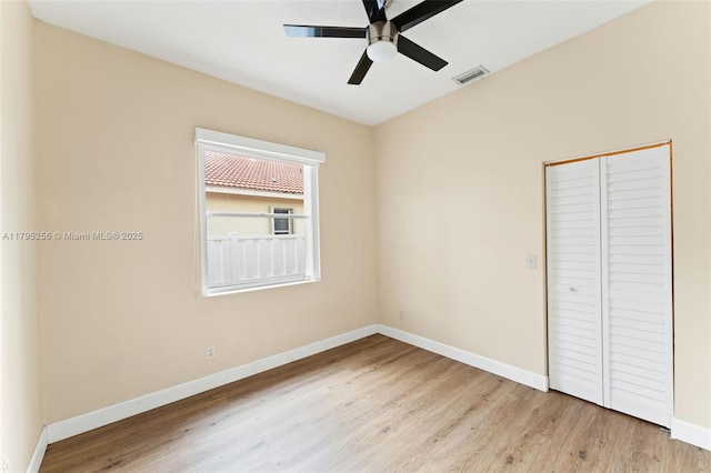 unfurnished bedroom with a closet, wood finished floors, visible vents, a ceiling fan, and baseboards