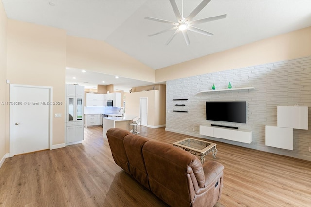 living area featuring baseboards, vaulted ceiling, light wood-style flooring, and a ceiling fan