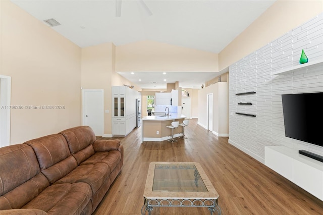 living area featuring visible vents, vaulted ceiling, light wood finished floors, a ceiling fan, and baseboards