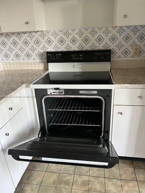 room details with decorative backsplash, electric range oven, white cabinets, and light countertops