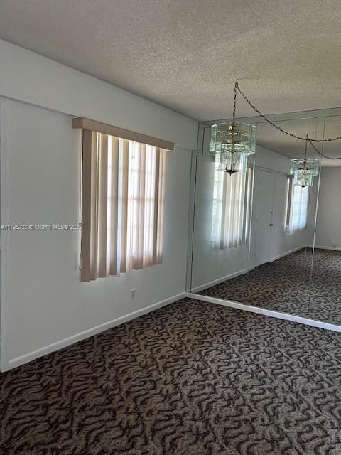 unfurnished dining area featuring carpet floors, a textured ceiling, and baseboards