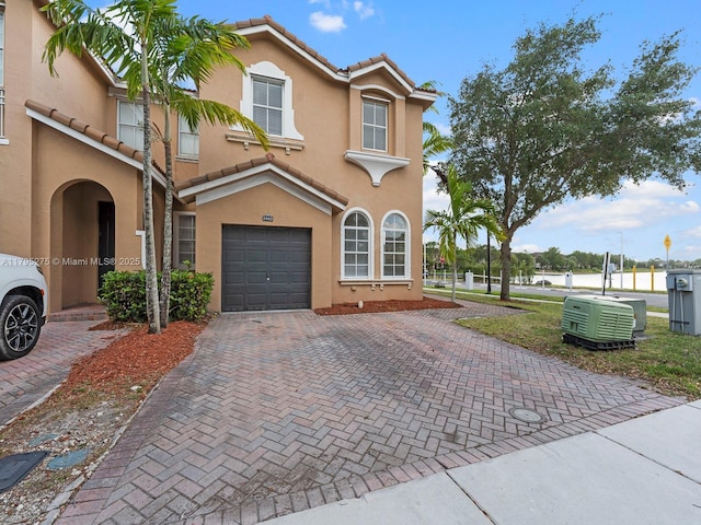 mediterranean / spanish-style house with a garage, stucco siding, a tiled roof, and decorative driveway