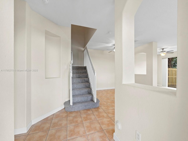 stairway with arched walkways, ceiling fan, and tile patterned flooring