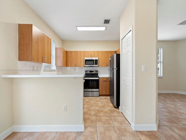 kitchen featuring appliances with stainless steel finishes, light countertops, a peninsula, light tile patterned floors, and visible vents