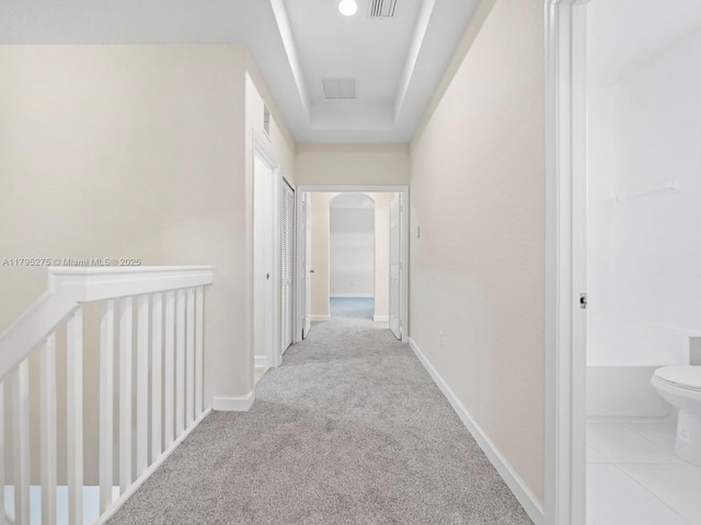 hallway with baseboards, carpet flooring, a raised ceiling, and visible vents