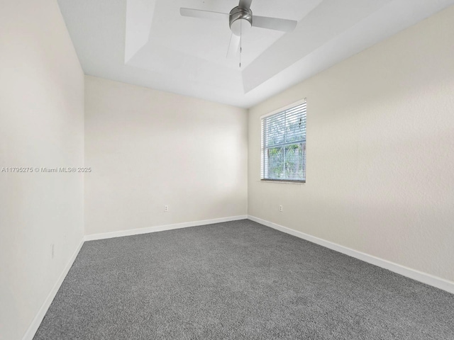 unfurnished room with dark colored carpet, baseboards, ceiling fan, and a tray ceiling