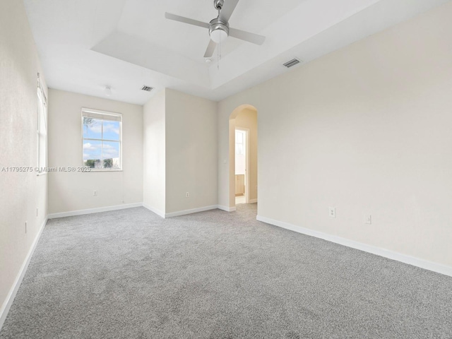unfurnished room with visible vents, a ceiling fan, a raised ceiling, arched walkways, and carpet
