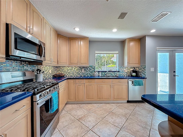 kitchen with appliances with stainless steel finishes, light brown cabinetry, dark countertops, a sink, and a textured ceiling