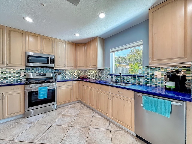 kitchen featuring stainless steel appliances, a sink, dark countertops, light brown cabinets, and decorative backsplash
