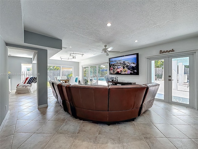 living room featuring a textured ceiling, healthy amount of natural light, a ceiling fan, baseboards, and french doors