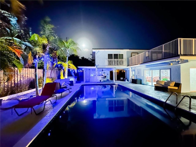 pool at night featuring fence and a patio