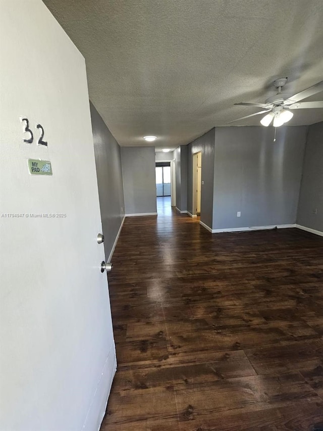 spare room with a textured ceiling, ceiling fan, dark wood finished floors, and baseboards