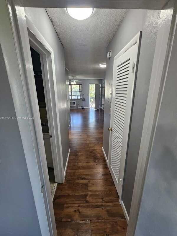 corridor featuring baseboards, a textured ceiling, and dark wood finished floors