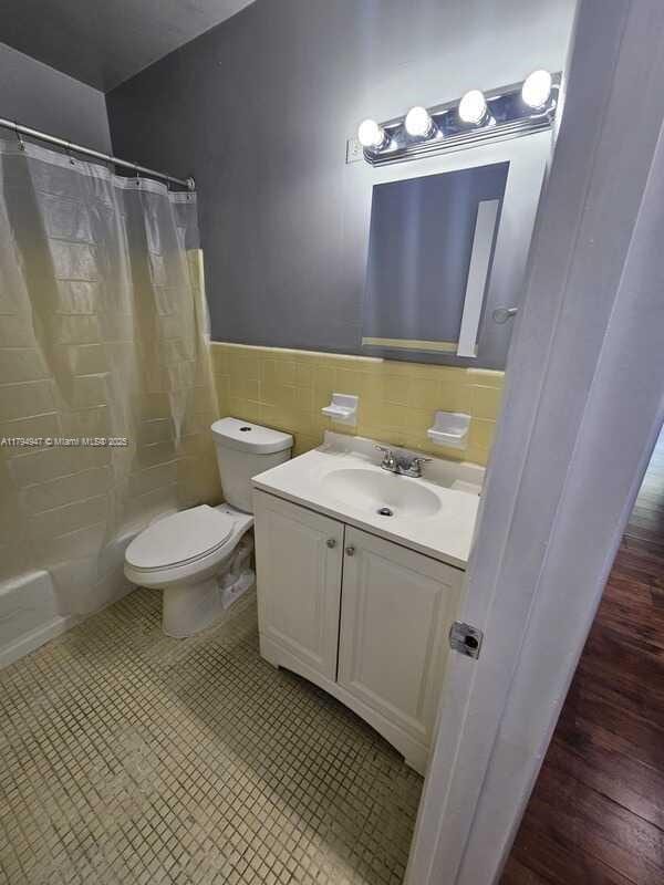full bath with toilet, tile walls, wainscoting, and vanity