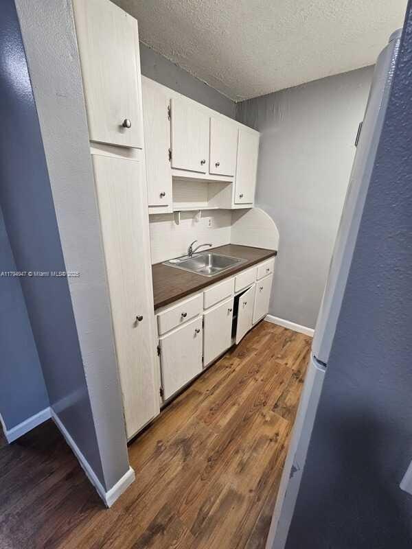 kitchen with a textured ceiling, dark countertops, a sink, freestanding refrigerator, and dark wood-style floors