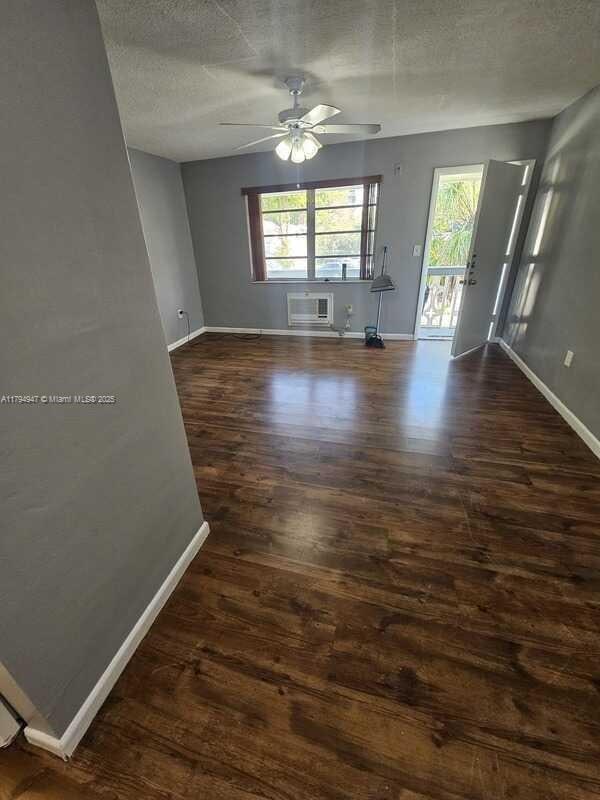 spare room featuring baseboards, a ceiling fan, dark wood-style floors, and a wealth of natural light