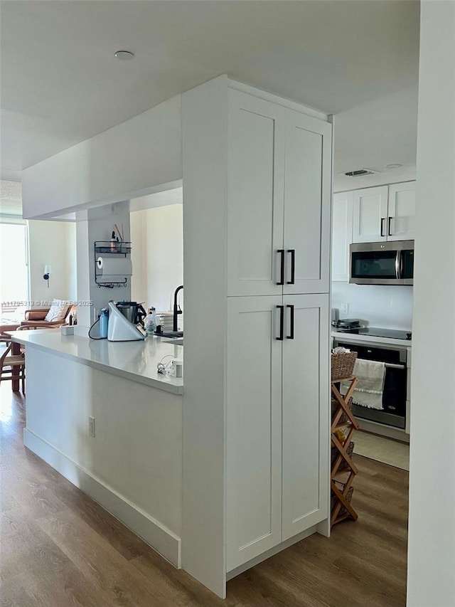 2101 Brickell Ave Unit 3208, Miami, FL 33129 - kitchen featuring appliances with stainless steel finishes, wood finished floors, light countertops, a sink, and white cabinetry